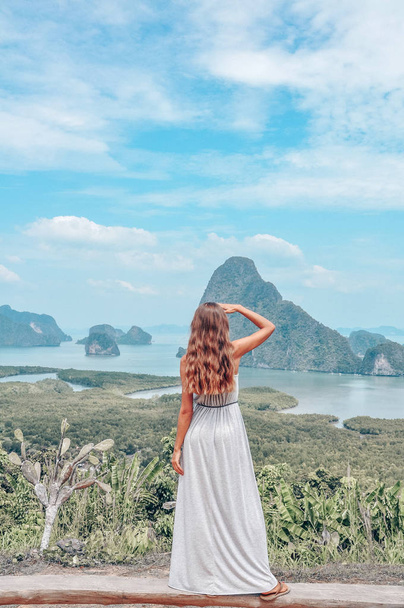 series traveling girl in Asia. beautiful girl with long dark hair in elegant grey dress staying on the top of hill with fantastic panoramic view on beautiful Thai bay - Photo, image