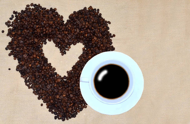 Λευκό φλιτζάνι καφέ και ένα καφέ φασόλια στο σχήμα της καρδιάς σε φύση πανί λινό φόντο. - Φωτογραφία, εικόνα