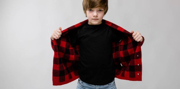 Nice preteen caucasian boy in casual outfit, stretching out his checkered shirt and showing different expressions on white wall in studio. - Photo, Image