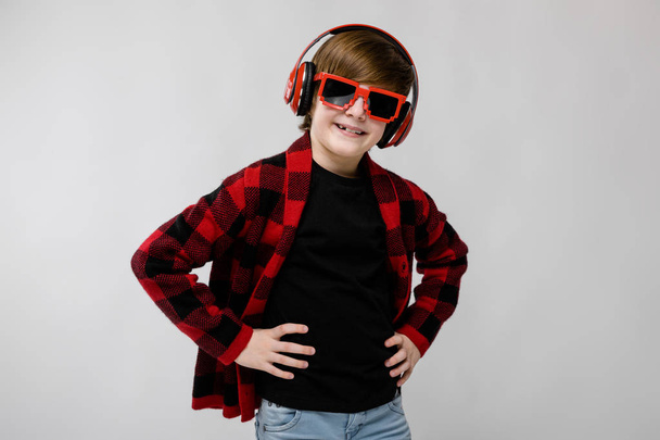 Kedves preteen kaukázusi fiú alkalmi ruhában, piros fejhallgató és napszemüveg mutatja a különböző kifejezések fehér falon a stúdió. - Fotó, kép