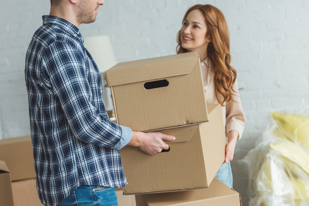partial view of smiling woman and husband holding cardboard boxes together at new apartment, moving home concept - Foto, afbeelding