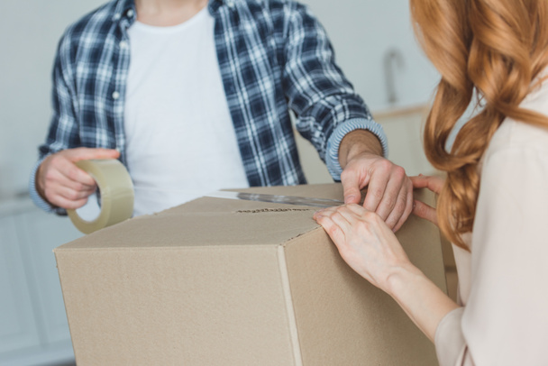 cropped shot of couple packing cardboard box with sticky tape together, relocation concept - Photo, Image