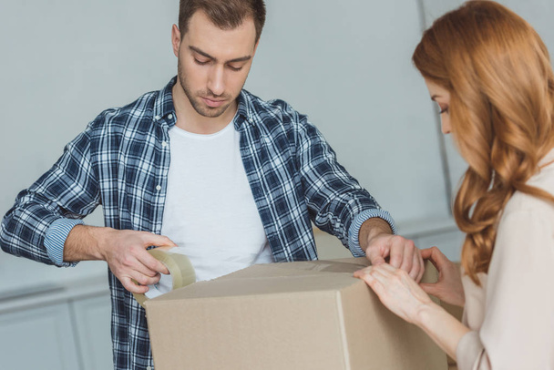 couple packing cardboard box with sticky tape together, relocation concept - Photo, Image