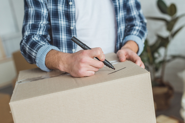 cropped shot of man signing cardboard box for moving home, relocation concept - 写真・画像