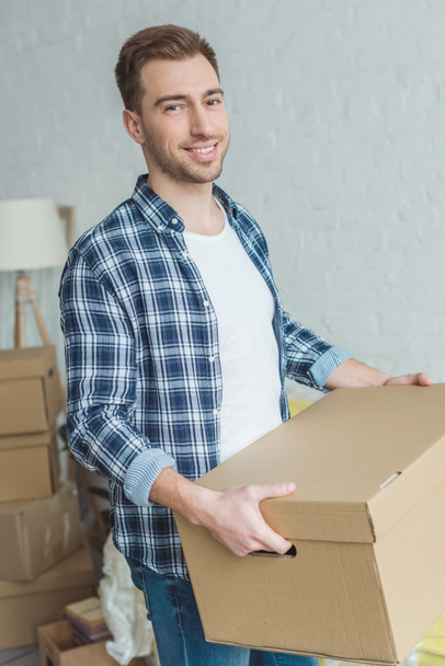 smiling man with cardboard box in hands at new home, relocation concept - Fotoğraf, Görsel