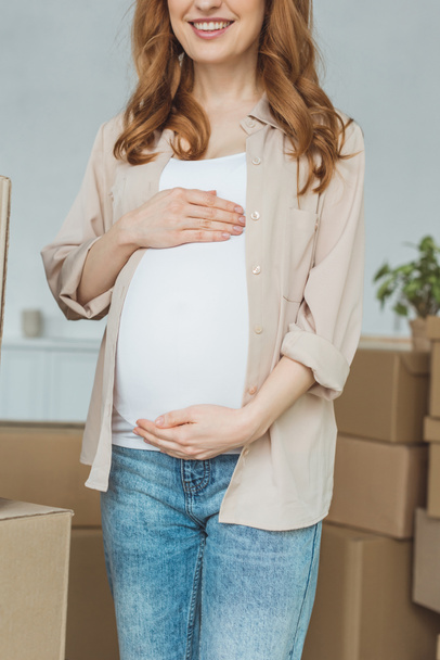 περικοπεί το πλάνο της χαμογελώντας έγκυος γυναίκα στο νέο διαμέρισμα, η έννοια της μετεγκατάστασης - Φωτογραφία, εικόνα