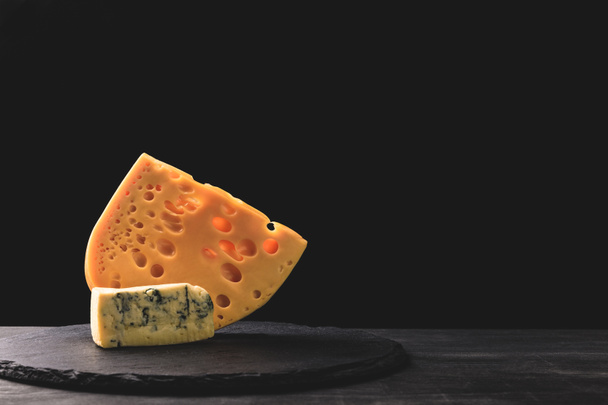 Close up view of emmental and blue cheese on board on black - Фото, изображение