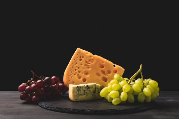 Blue cheese and emmental on board with grapes on black - Φωτογραφία, εικόνα