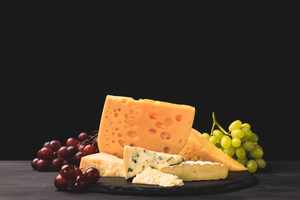 Different types of cheese on board with grapes on black  - 写真・画像