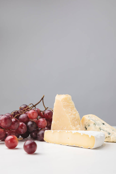 Brie, cheddar and blue cheese with grapes on gray - Fotoğraf, Görsel