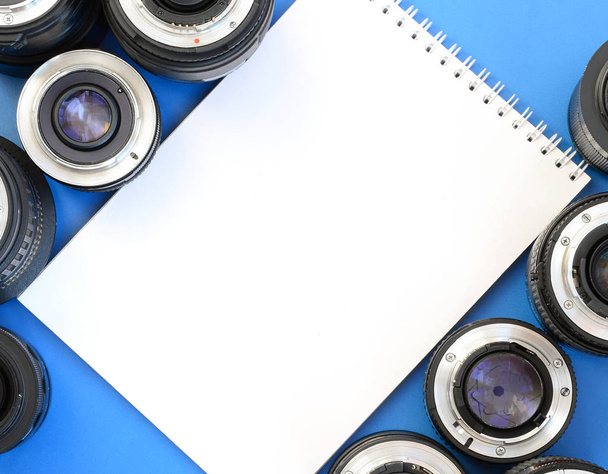 Varios lentes fotográficos y cuaderno blanco se encuentran sobre un fondo azul brillante. Espacio para texto
 - Foto, Imagen