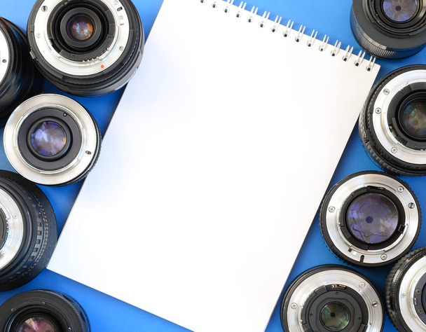 Кілька фотографічних лінз і білий блокнот лежать на яскраво-блакитному тлі. Простір для тексту
 - Фото, зображення