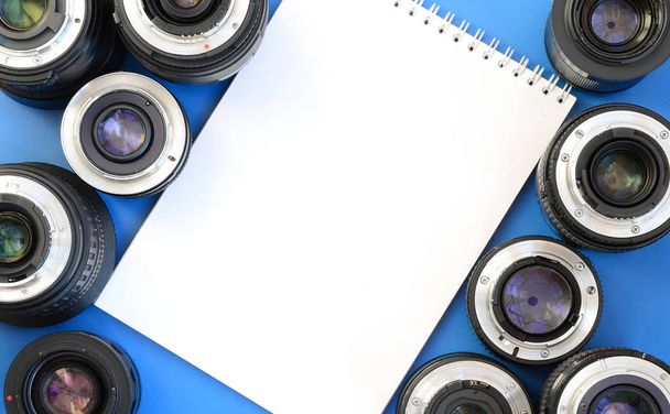 Verschillende fotografische lenzen en witte laptop liggen op een heldere blauwe achtergrond. Ruimte voor tekst - Foto, afbeelding