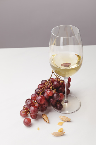 Vista da vicino del bicchiere di vino bianco, uva e mandorla su grigio
 - Foto, immagini