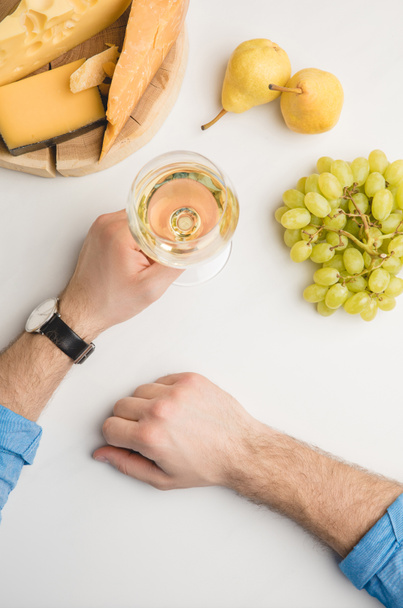 Immagine ritagliata dell'uomo con bicchiere di vino, diversi tipi di formaggio su tavola di legno e frutta su bianco
 - Foto, immagini