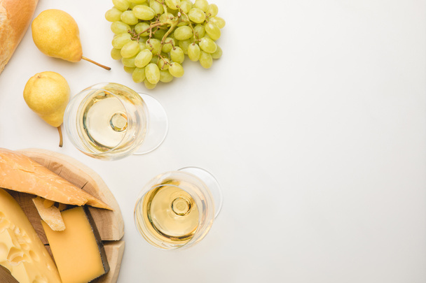 Top view of different types of cheese on wooden board, wineglasses and fruits on white - Photo, Image