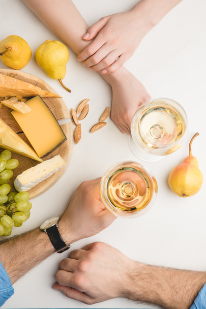 白ワイングラス、さまざまな種類のチーズ、梨、ブドウ、アーモンドとカップルのトップ ビュー  - 写真・画像