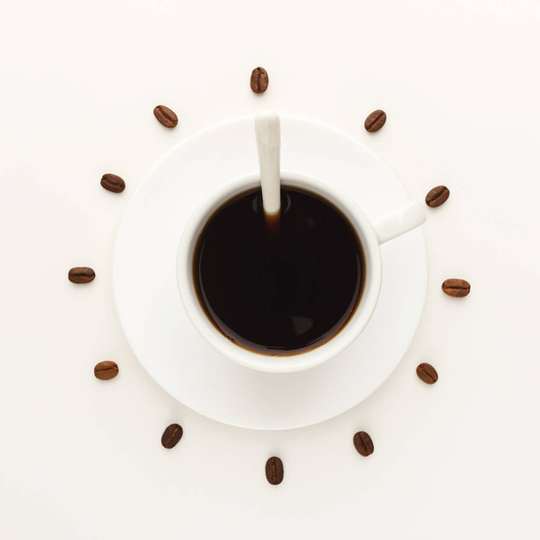 Taza de café negro y frijoles tostados formando esfera de reloj aislado en blanco
 - Foto, Imagen