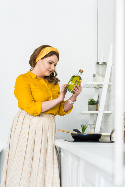 όμορφη γυναίκα βλέπει μπουκάλι ελαιόλαδο στην κουζίνα - Φωτογραφία, εικόνα