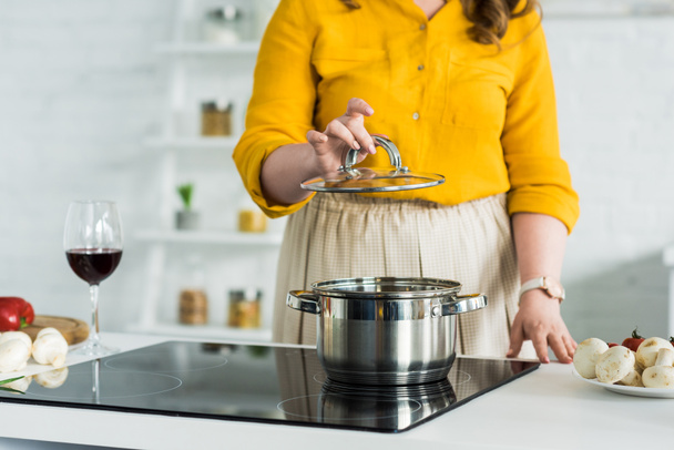 cropped image of woman holding lid from pan near electric stove in kitchen - 写真・画像
