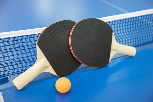 Bola naranja para tenis de mesa y dos raquetas de rojo y negro co
 - Foto, Imagen