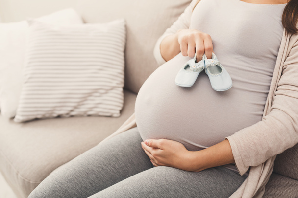 Έγκυος γυναίκα κρατώντας μικροσκοπικά παπούτσια κοντά κοιλιά - Φωτογραφία, εικόνα
