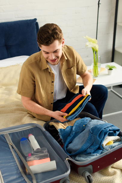 handsome smiling man packing clothes for vacation - Valokuva, kuva