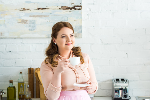beautiful woman drinking coffee and looking away in kitchen - Fotó, kép