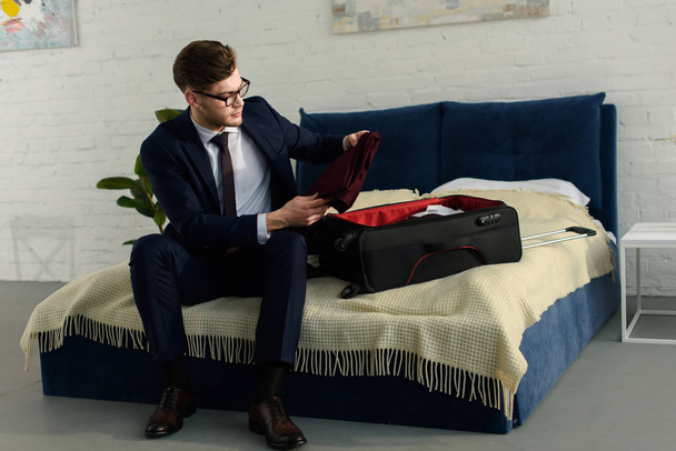handsome businessman in suit packing bag for business trip - Фото, зображення