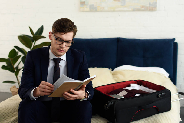 handsome businessman in suit reading diary while preparing for business trip - Foto, Imagem