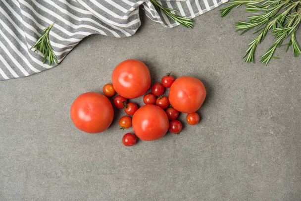 vista superior de tomates frescos maduros sobre una superficie de hormigón gris con lino y romero
 - Foto, Imagen