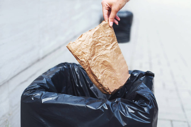 Close-up hand throwing a crumpled paper bag in trash can on the  - Photo, image