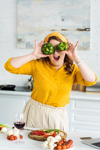 beautiful woman covering eyes with bell peppers at kitchen - Foto, immagini