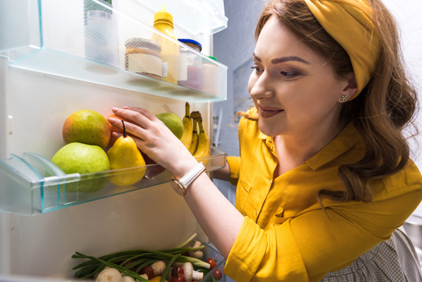 gyönyörű nő vesz gyümölcsök a hűtőszekrény a konyha - Fotó, kép