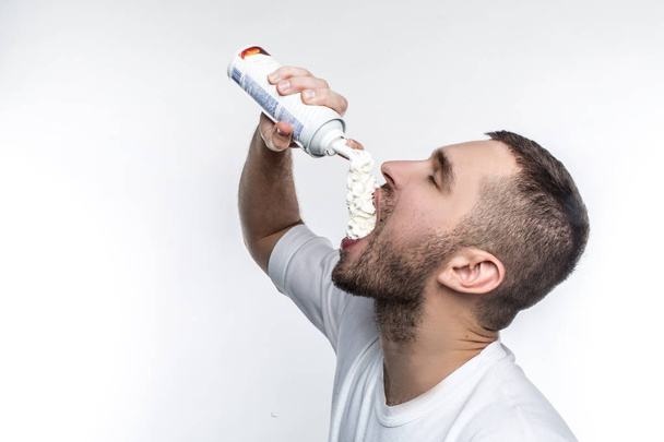 He likes sweet food among everything in a world. This man is putting some cream into his mouth with pleasure. He cant stop doing it. Isolated on white background. - Foto, afbeelding