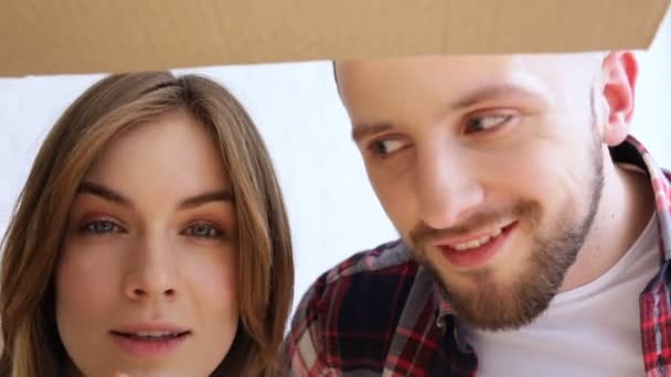 Happy young couple opening cardboard box and looking in it. Looking like something cute in it. - Imágenes, Vídeo