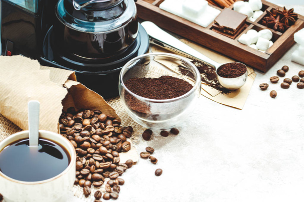Variety things for prepare coffee. Roasted beans, ground coffee, scoop, electric coffee machine and assortment of sweets and spices to eat with on light background. - Foto, afbeelding