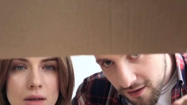 Happy young couple opening cardboard box and looking in it. - Video, Çekim