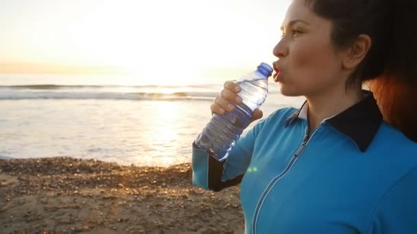 Nő iszik egy vizes palackot a naplemente, tenger közelében - Felvétel, videó