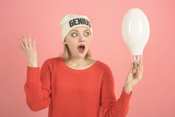 Idea and creative concept. Woman with confused expression has idea, pink background.Lady with surprised face holds lamp in hand, symbol of idea. Lady in hat with genius word, found out idea. - Foto, Bild