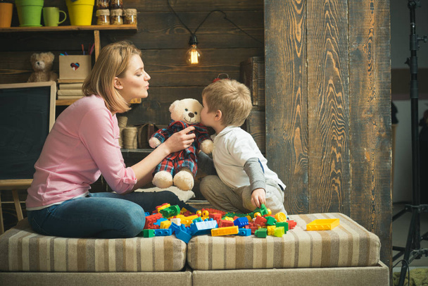 Mother teaches son to be kind and friendly. Kindness and education concept. Family play with teddy bear at home. Mom and child play with soft toy. Nursery with chalkboard on background. - Foto, imagen