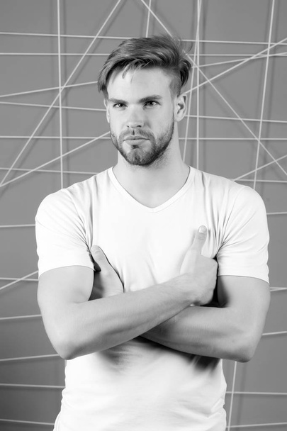 Macho with blond hair, stylish haircut. Hair care in salon or barbershop. Man in tshirt with folded hands. Guy with bearded unshaven face. Mens beauty and grooming, black and white - Foto, Imagem