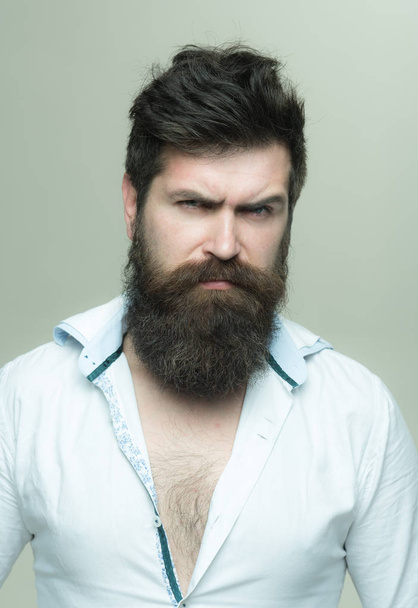Man with long beard, mustache and stylish hair, light background. Macho on strict face, wears unbuttoned shirt. Guy with modern hairstyle visited hairdresser. Barbershop or hairdresser concept. - Фото, изображение