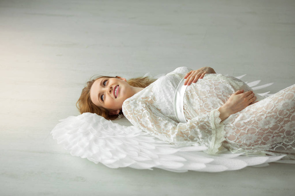 beautiful young pregnant girl with red hair in a lacy white dress lying on a light floor - Foto, Bild
