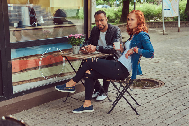 A couple dating drinking coffee, sitting near the coffee shop. Outdoors on a date. - Photo, image