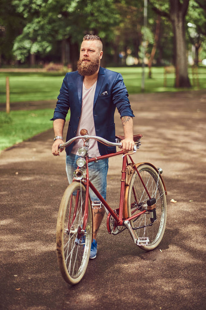 Mann in legerer Kleidung, der mit einem Retro-Fahrrad in einem Stadtpark spaziert. - Foto, Bild