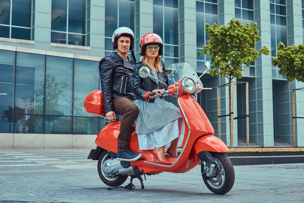 Een aantrekkelijk Stel, een knappe man en sexy vrouw rijden samen op een rode retro scooter in een stad. - Foto, afbeelding