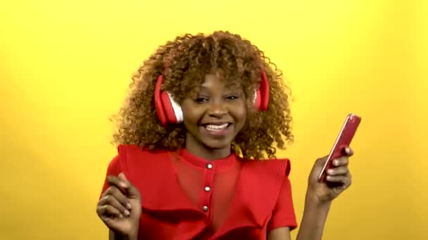 Girl of african american appearance in headphones sings songs. Yellow background - Felvétel, videó