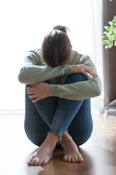 Unhappy lonely and depressed young woman hiding her face between legs at home. - Photo, Image