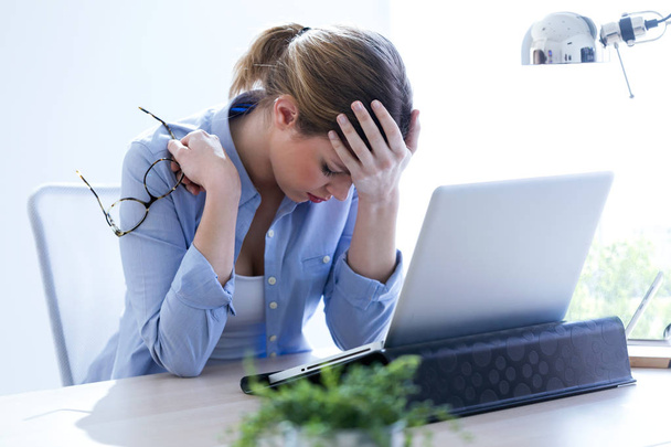 Dość młoda kobieta z bólem głowy za pomocą swojego laptopa w domu. - Zdjęcie, obraz